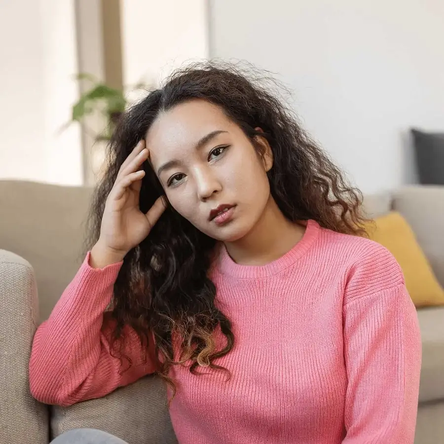 Worried young woman sitting thoughtfully at home, reflecting the challenges addressed by Ginger-U's stress and anxiety program, which offers strategies for coping and finding calm.