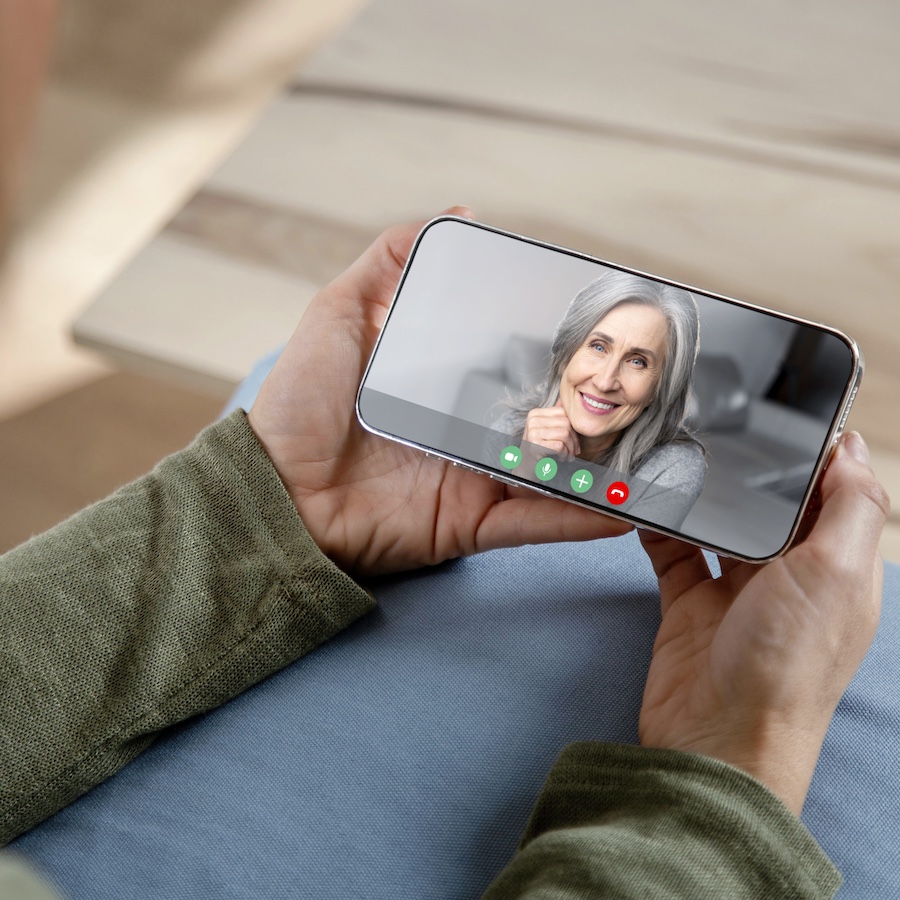 Woman holding a smartphone with a video call screen displaying a smiling woman, symbolizing Ginger-U's online health coaching sessions. 